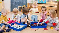 Eine Gruppe Kleinkinder spielt mit Behältern mit Sand und Kaffeebohnen.