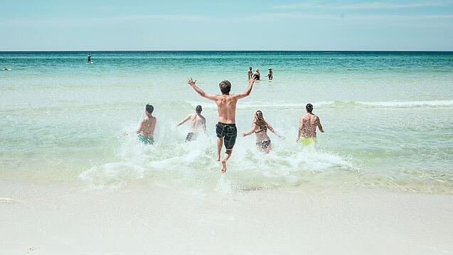 Mehrere Jugendliche laufen in Badeklamotten ins Meer.