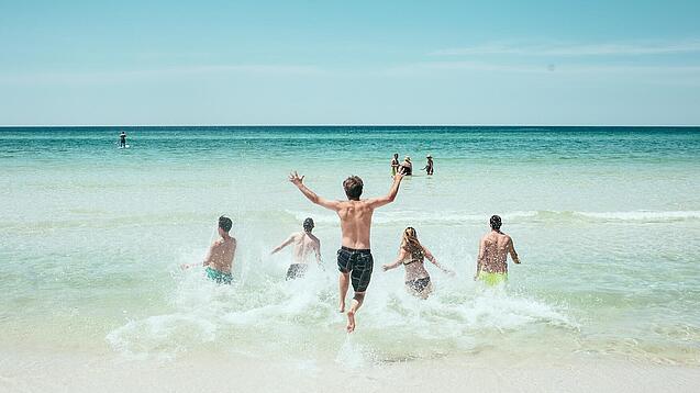 Mehrere Jugendliche laufen in Badeklamotten ins Meer.