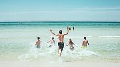 Mehrere Jugendliche laufen in Badeklamotten ins Meer.