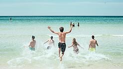 Mehrere Jugendliche laufen in Badeklamotten ins Meer.
