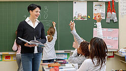 Eine Lehrerin steht vor einer Tafel, Schülerinnen melden sich.