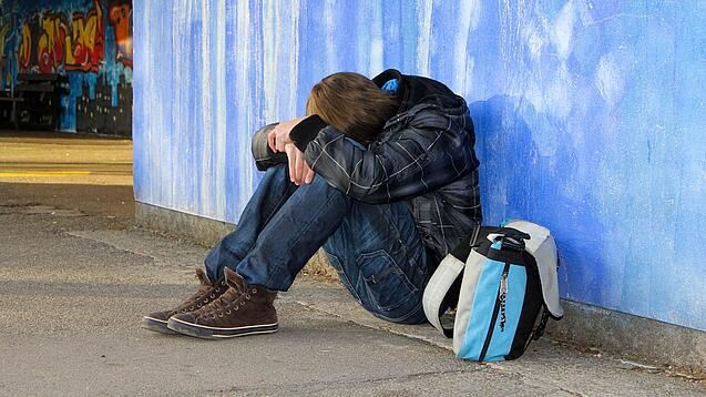 Junger Mann sitzt auf dem Boden und hat das Gesicht und die Hände auf den Knien abgelegt.