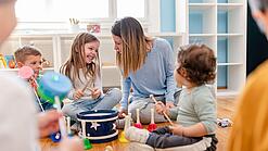 Kinder verschiedenen Alters und eine Erzieherin beschäftigen sich mit Musikinstrumenten.
