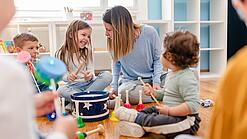 Kinder verschiedenen Alters und eine Erzieherin beschäftigen sich mit Musikinstrumenten.