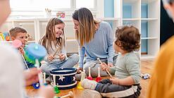 Kinder verschiedenen Alters und eine Erzieherin beschäftigen sich mit Musikinstrumenten.