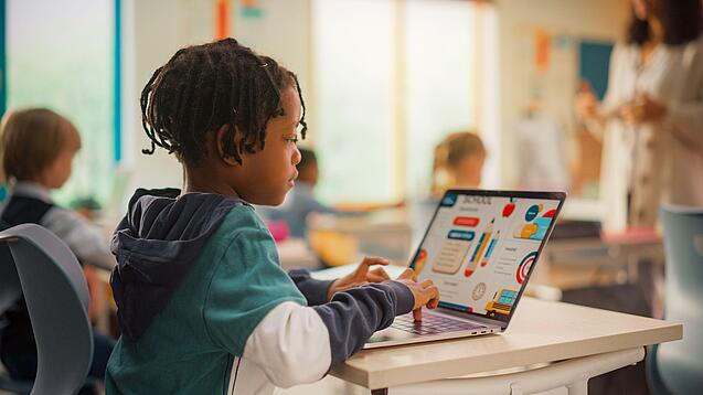 Ein Junge sitzt in einem Klassenzimmer vor einem Laptop.