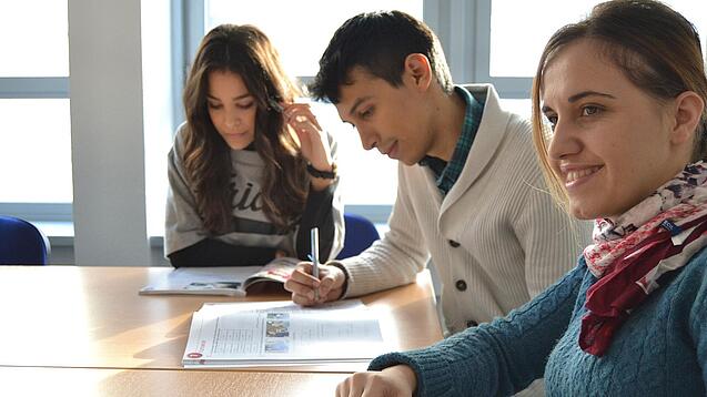 Lernende sitzen an einem Tisch und arbeiten in ihren Heften. 