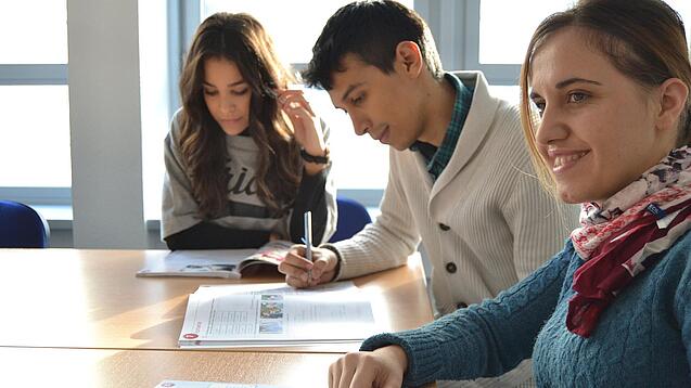 Lernende sitzen an einem Tisch und arbeiten in ihren Heften. 