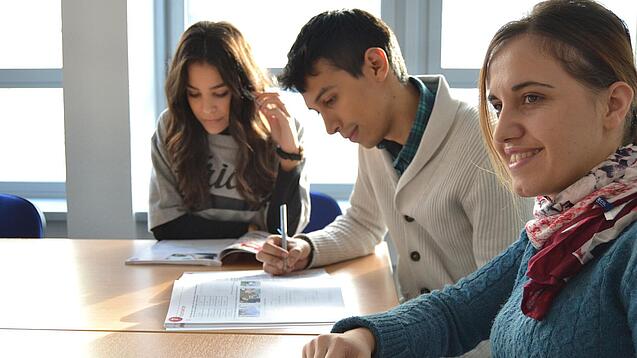 Lernende sitzen an einem Tisch und arbeiten in ihren Heften. 