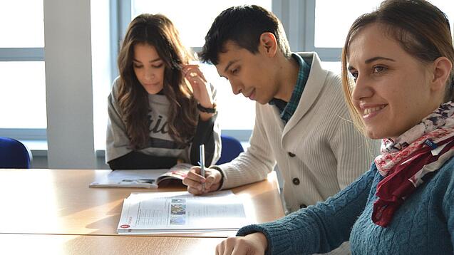 Lernende sitzen an einem Tisch und arbeiten in ihren Heften. 