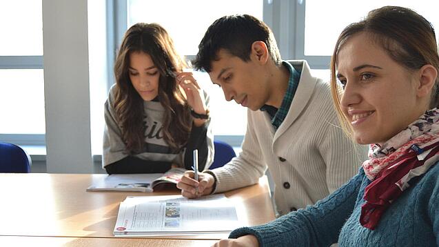 Lernende sitzen an einem Tisch und arbeiten in ihren Heften. 