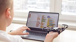 Ein Junge sitzt an einem Laptop und programmiert einen Flugroboter.