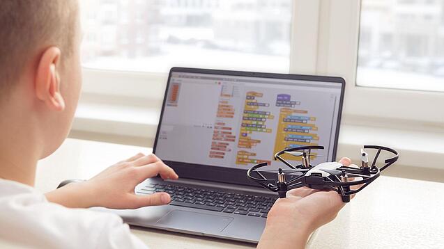 Ein Junge sitzt an einem Laptop und programmiert einen Flugroboter.