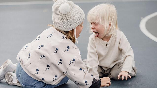 Zwei Kleinkinder schneiden sich gegenseitig Grimassen.