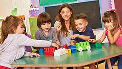 Eine pädagogische Fachkraft spielt in einer Kita mit Kindern an einem Tisch.