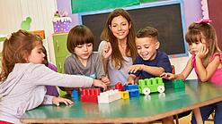 Eine pädagogische Fachkraft spielt in einer Kita mit Kindern an einem Tisch.