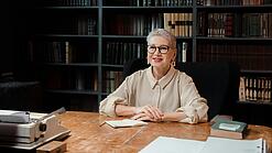 Frau sitzt in einem Büro an einem Schreibtisch und lächelt in die Kamera.
