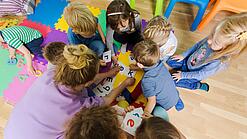 Eine Erzieherin sitzt mit Kindergartenkindern in einem Kreis und schaut auf Buchstaben. 