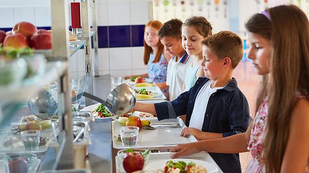 Mehrere Schüler:innen stehen an einem Buffet und bedienen sich beim Essen.