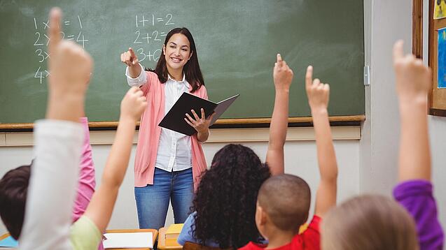 Eine Lehrerin steht in einem Klassenzimmer.