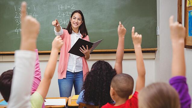 Eine Lehrerin steht in einem Klassenzimmer.