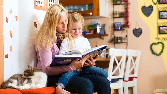 Frau liest dem Kind auf ihrem Schoß ein Buch vor