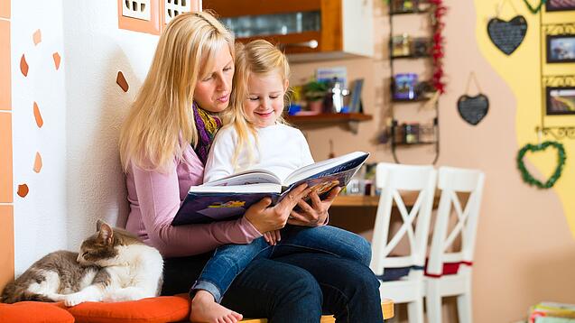Frau liest dem Kind auf ihrem Schoß ein Buch vor