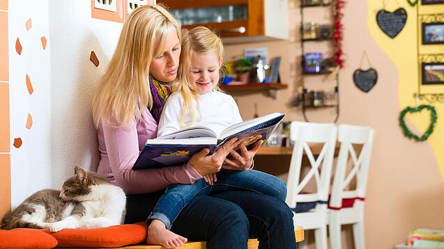 Frau liest dem Kind auf ihrem Schoß ein Buch vor