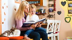 Frau liest dem Kind auf ihrem Schoß ein Buch vor