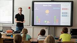 Ein Lehrer steht an einem Smartboard vor einer Klasse. 