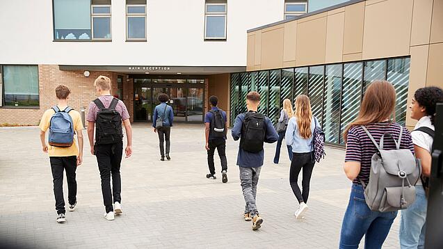 Eine Gruppe Schüler läuft auf ein Schulgebäude im Hintergrund zu.