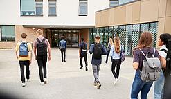 Eine Gruppe Schüler läuft auf ein Schulgebäude im Hintergrund zu.