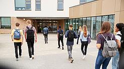 Eine Gruppe Schüler läuft auf ein Schulgebäude im Hintergrund zu.