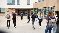 Eine Gruppe Schüler läuft auf ein Schulgebäude im Hintergrund zu.