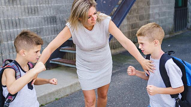 Eine Frau hält zwei Kinder zurück, die sich mit erhobenen Fäusten gegenüberstehen. 