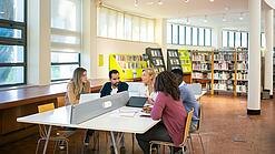 Eine Gruppe Dozierender und Studierender in einer Bibliothek.