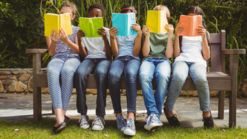 Fünf Kinder lesen Bücher auf einer Parkbank.