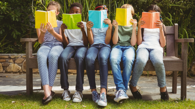 Fünf Kinder lesen Bücher auf einer Parkbank.