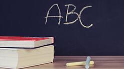 Schulbücher vor einer Tafel in einem Klassenzimmer.