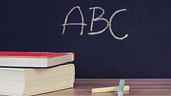 Schulbücher vor einer Tafel in einem Klassenzimmer.