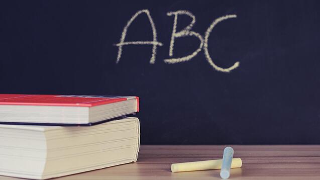 Schulbücher vor einer Tafel in einem Klassenzimmer.