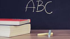Schulbücher vor einer Tafel in einem Klassenzimmer.