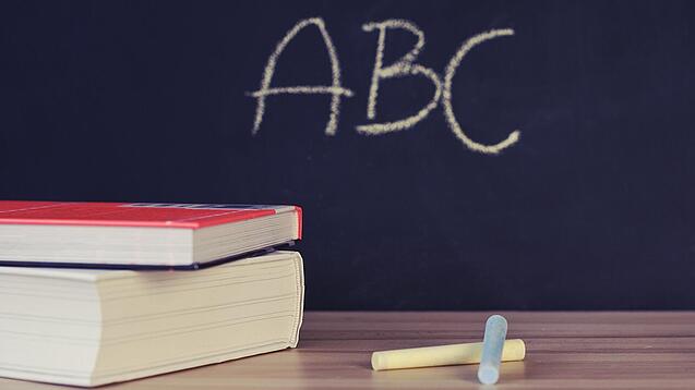 Schulbücher vor einer Tafel in einem Klassenzimmer.