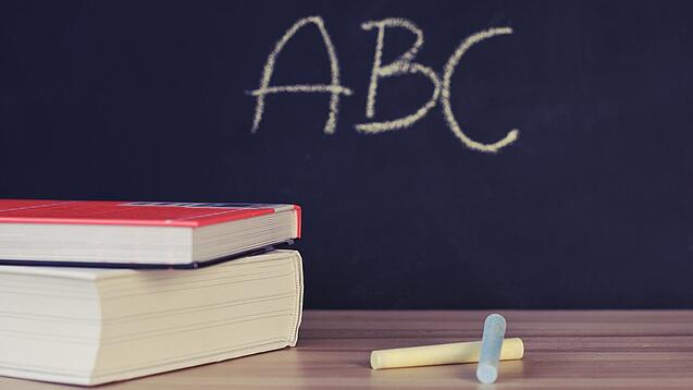 Schulbücher vor einer Tafel in einem Klassenzimmer.