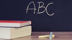 Schulbücher vor einer Tafel in einem Klassenzimmer.