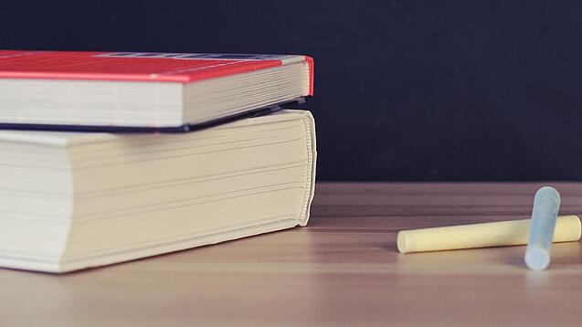 Schulbücher vor einer Tafel in einem Klassenzimmer.