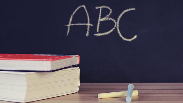 Schulbücher vor einer Tafel in einem Klassenzimmer.