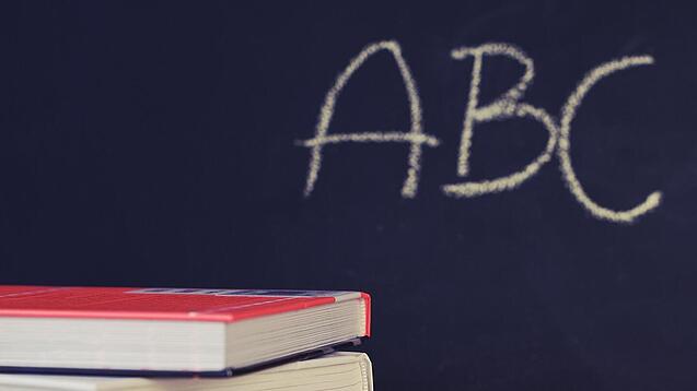 Schulbücher vor einer Tafel in einem Klassenzimmer.