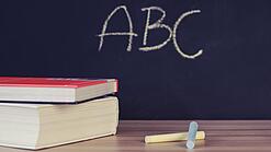 Schulbücher vor einer Tafel in einem Klassenzimmer.
